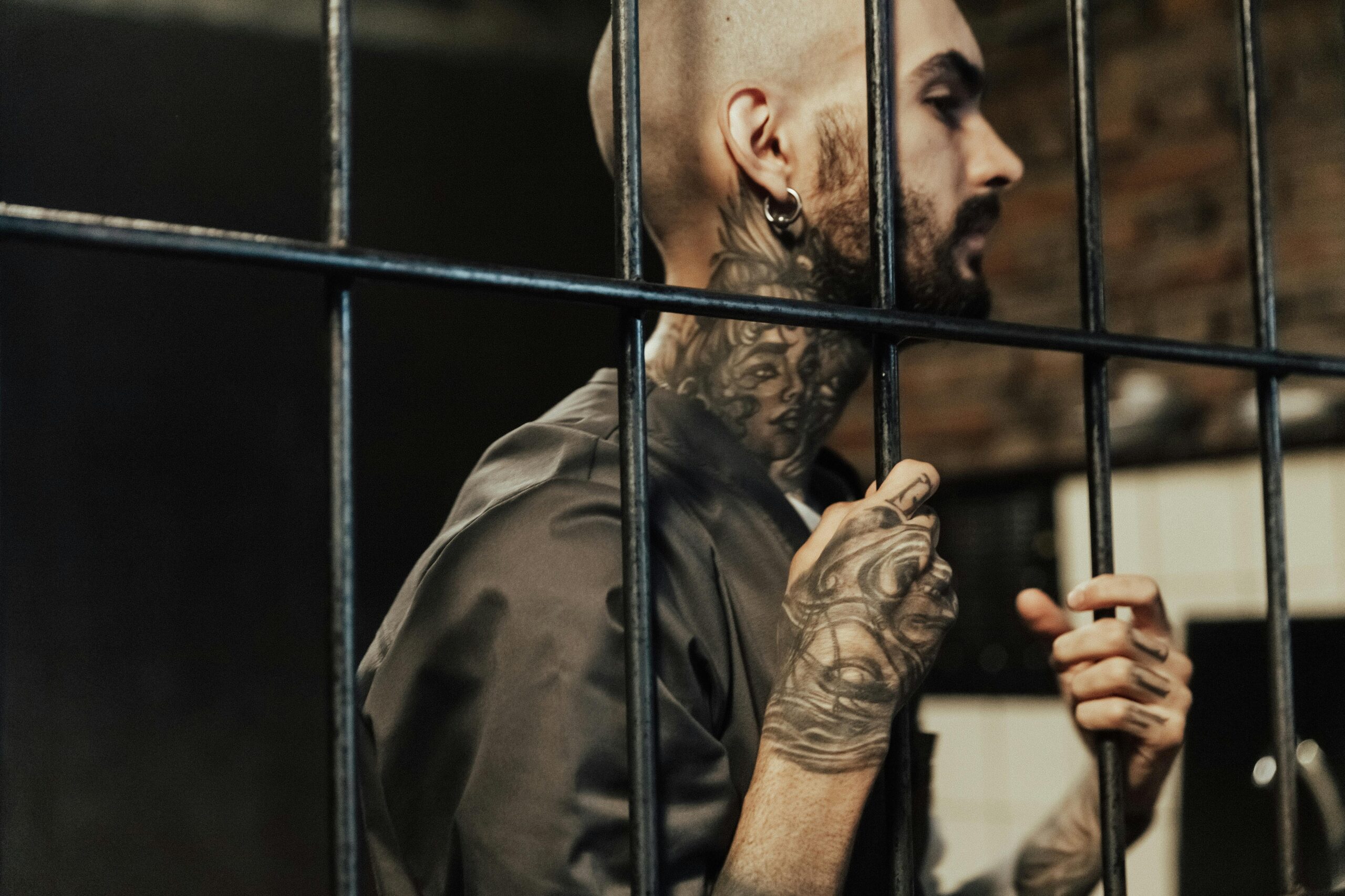 A tattooed man behind prison bars, contemplating life inside a penitentiary.