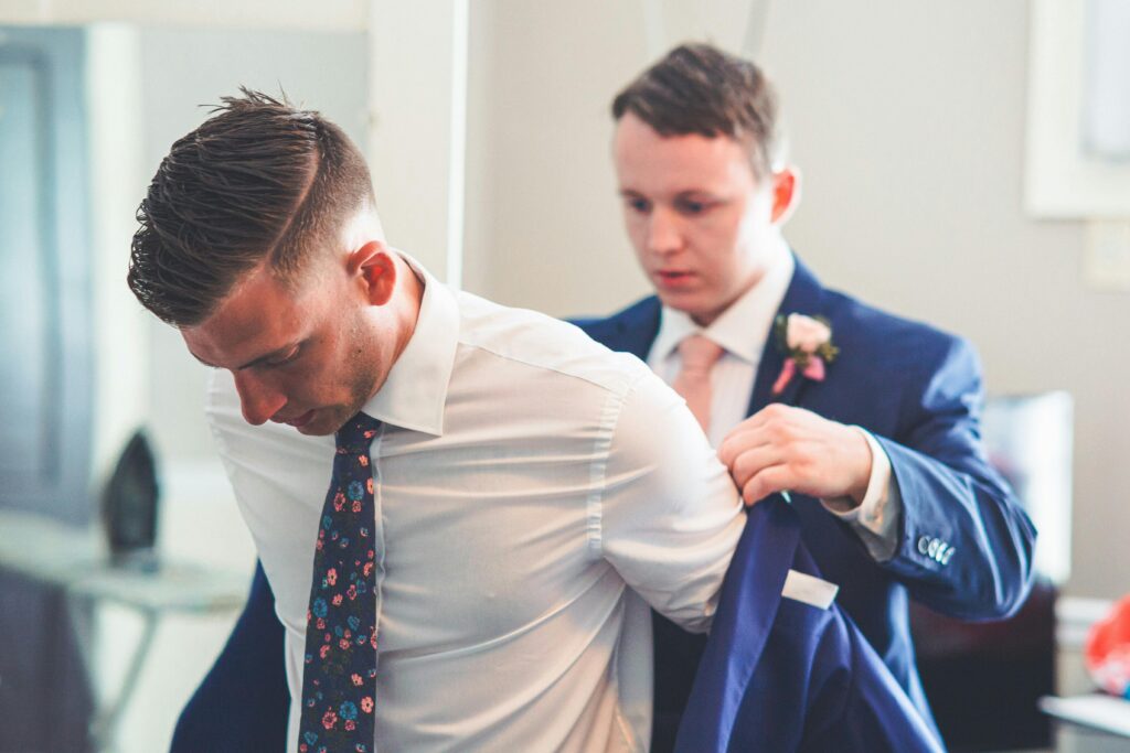 A groom gets assistance with his jacket from the best man on his wedding day.