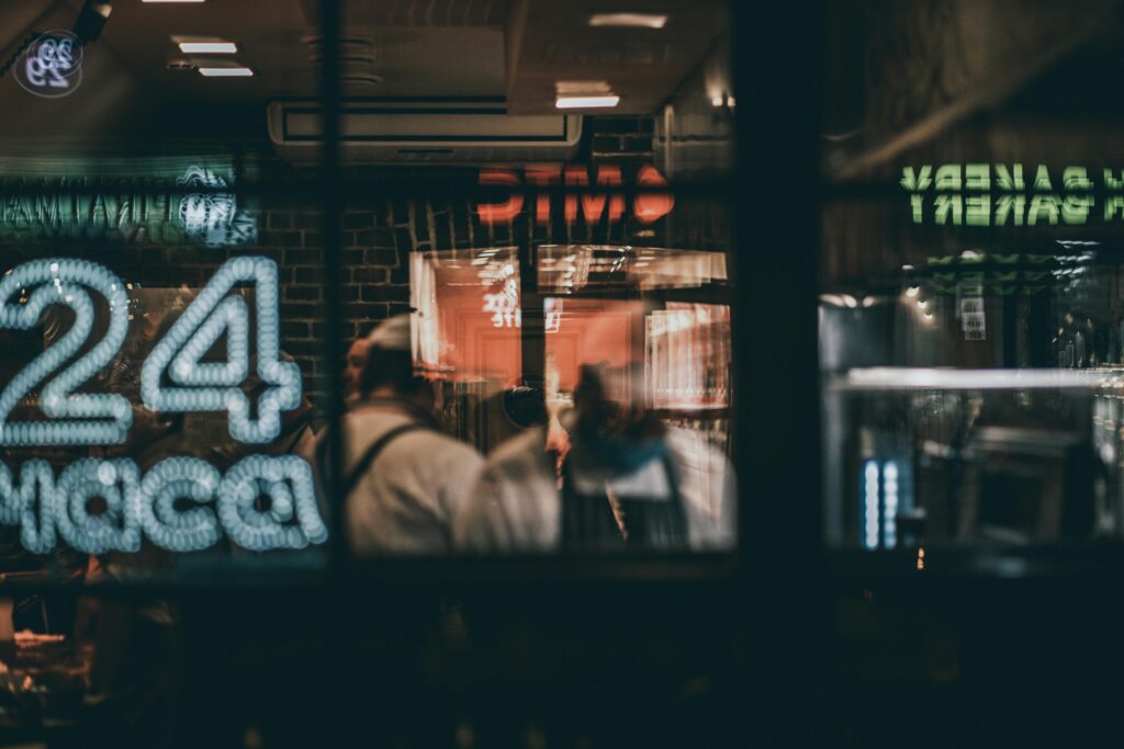 Blurred view through cafe window, capturing a night scene with people inside. Warm, inviting atmosphere.