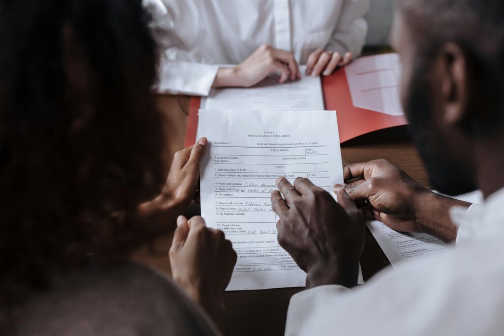 A couple collaboratively signs legal documents in the presence of an advisor.